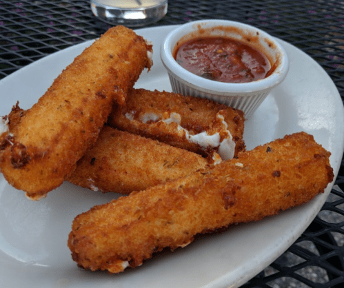Four golden-brown mozzarella sticks on a plate, served with a small cup of marinara sauce.