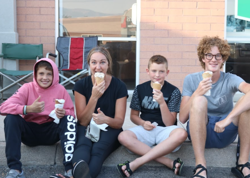Four kids sitting on a curb, enjoying ice cream cones and smiling at the camera.