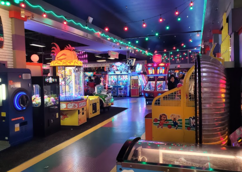A vibrant arcade filled with colorful games, bright lights, and playful decorations, bustling with people.
