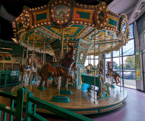A colorful carousel with ornate decorations and various animals, set indoors with large windows in the background.