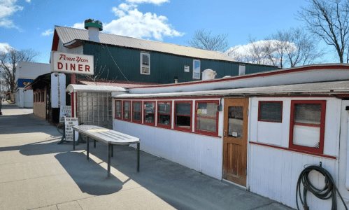 Exterior of Penn Yan Diner, featuring a white and red building with a table outside and a blue sky in the background.