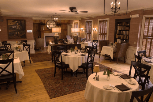 Cozy restaurant interior with elegantly set tables, warm lighting, and a fireplace, creating an inviting atmosphere.