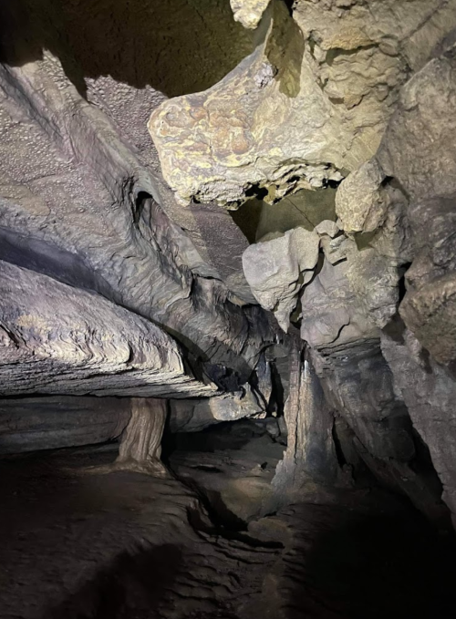 A dimly lit cave interior with textured rock formations and a narrow path leading deeper into the cave.