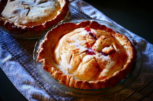 Two freshly baked fruit pies cooling on a wire rack, with golden crusts and a hint of filling peeking through.