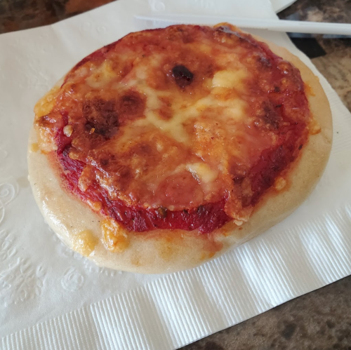 A small, round pizza with melted cheese and a slightly crispy crust, resting on a napkin.