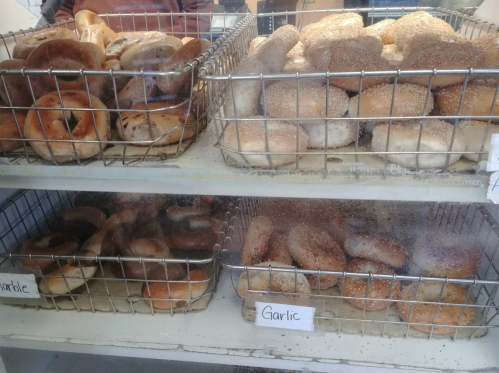 Two wire baskets filled with assorted bagels, labeled "Garlic" and "Cinnamon," on a display shelf.