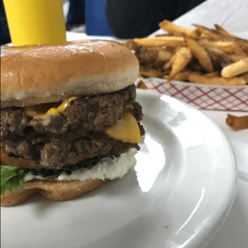 A close-up of a double cheeseburger with lettuce, cheese, and sauce, served with a side of fries.