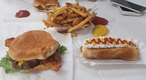 A burger with lettuce, cheese, and bacon, a hot dog with ketchup and mustard, and a side of fries with condiments.