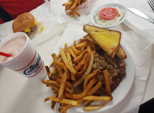 A plate of fries and a meat dish, with a side of toast, a burger, and a drink on a table.