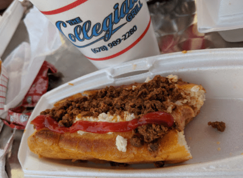 A hot dog topped with ground meat and ketchup, served on a styrofoam tray with a drink in the background.