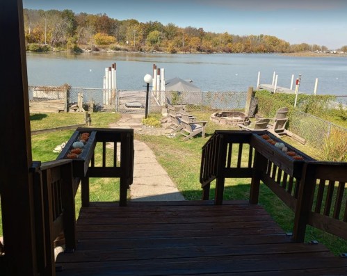 View from a wooden deck overlooking a calm river with autumn trees and a small dock in the background.