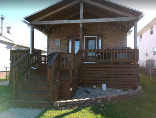 A wooden house with a porch, steps, and a landscaped yard, featuring a stone pathway and decorative elements.