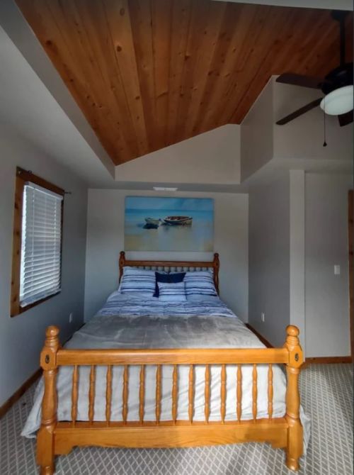 Cozy bedroom with a wooden bed, striped bedding, and a ceiling fan, featuring a scenic painting above the bed.