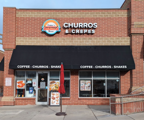 Exterior of a restaurant named "Churros & Crepes," featuring a sign and outdoor seating area.