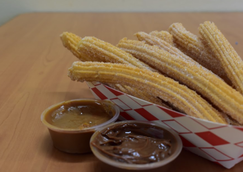 A basket of golden churros dusted with sugar, accompanied by two dipping sauces: caramel and chocolate.