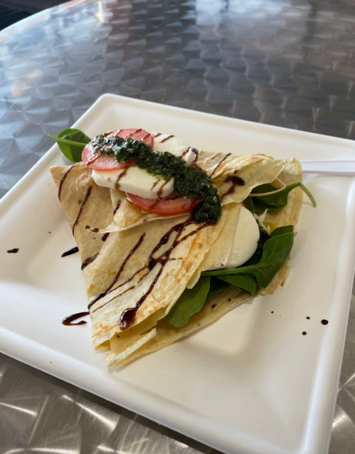 A plate with a folded crepe filled with spinach, tomato, and drizzled with pesto and balsamic glaze.
