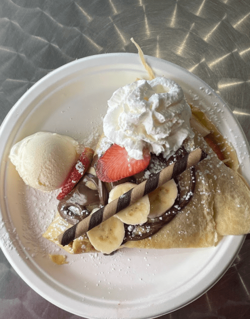 A delicious crepe topped with whipped cream, strawberries, bananas, chocolate sauce, and a scoop of vanilla ice cream.