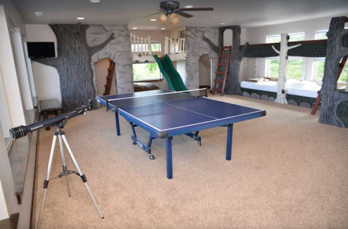 A spacious playroom featuring a ping pong table, treehouse beds, a slide, and a telescope.