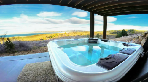 A hot tub on a patio overlooking a scenic landscape with water and hills under a blue sky.