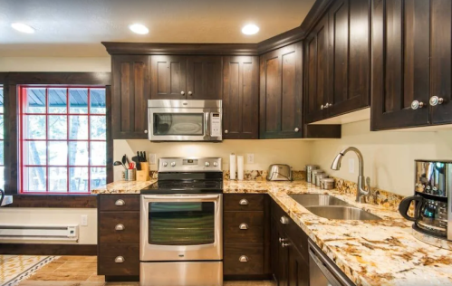 Modern kitchen with dark wood cabinets, stainless steel appliances, and a granite countertop. Bright window with red accents.