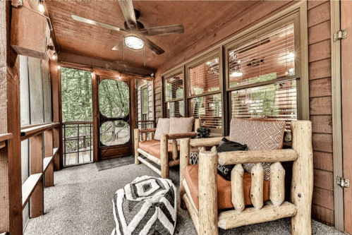 Cozy screened porch with wooden furniture, a ceiling fan, and large windows overlooking greenery.