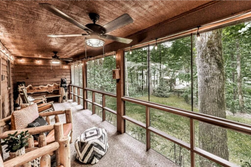 Cozy screened porch with wooden decor, comfortable seating, and a view of a lush green forest outside.