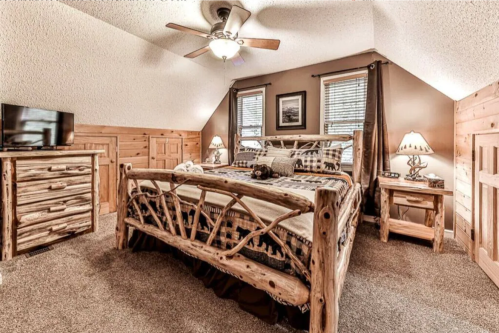 Cozy attic bedroom with a wooden bed, dresser, and nightstand, featuring warm lighting and rustic decor.