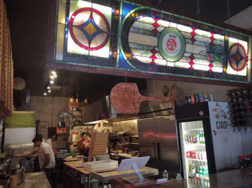 Interior of a restaurant kitchen with stained glass decor, featuring chefs at work and a display of beverages.