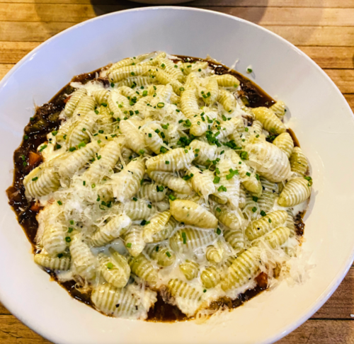 A bowl of pasta with green-striped gnocchi topped with cheese and herbs in a rich sauce.