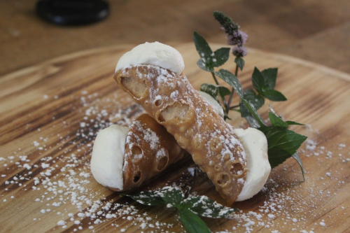 Two cannoli filled with cream, dusted with powdered sugar, on a wooden board with mint leaves.