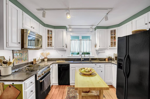 Bright kitchen with white cabinets, stainless steel appliances, a wooden table, and a bowl of fruit on the counter.