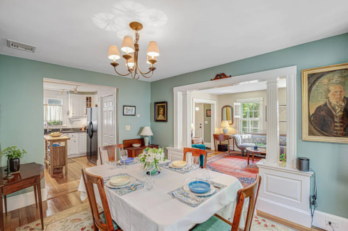 A cozy dining room with a table set for four, featuring a chandelier and views into adjacent rooms.