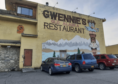 Exterior of Gwennie's Old Alaska Restaurant, featuring a colorful mural and parked cars in front.