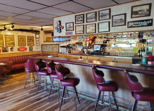 A cozy bar area with red leather stools, a wooden counter, and vintage decor on the walls.