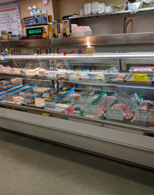 A display case filled with various meats and prepared foods, decorated with a "Happy Holidays" sign.