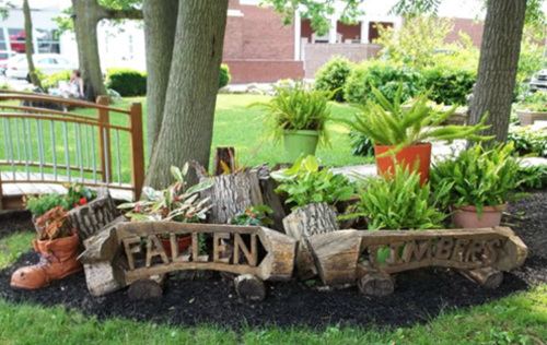A garden display featuring wooden logs with the words "Fallen Timbers," surrounded by plants and greenery.