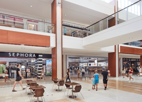 A modern shopping mall interior with stores, shoppers, and seating areas. Bright and spacious atmosphere.
