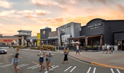 A bustling shopping area with various restaurants and cafes, featuring people walking along the street at sunset.