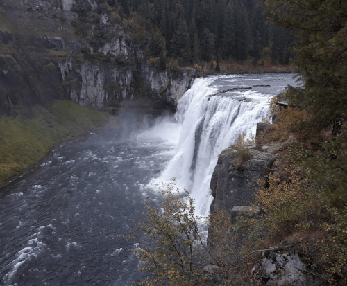A majestic waterfall cascading over rocky cliffs into a river, surrounded by lush greenery and mist.