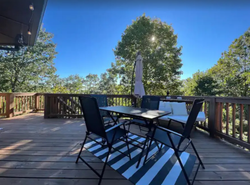 A sunny deck with a table and chairs, surrounded by trees and a clear blue sky.