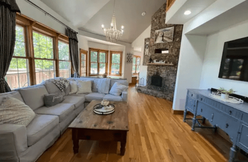 Cozy living room with a large sectional sofa, wooden coffee table, stone fireplace, and bright windows.