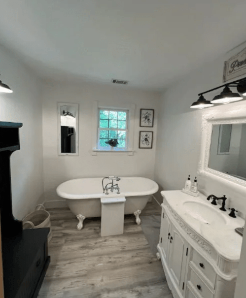 A bright bathroom featuring a freestanding bathtub, a vintage vanity, and natural light from a window.