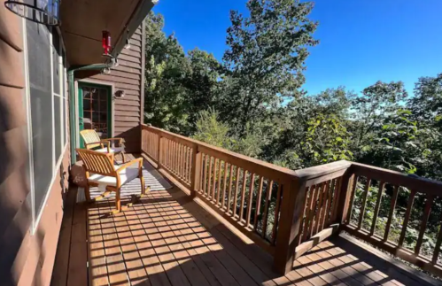 A wooden deck with two chairs overlooks a lush green landscape under a clear blue sky.
