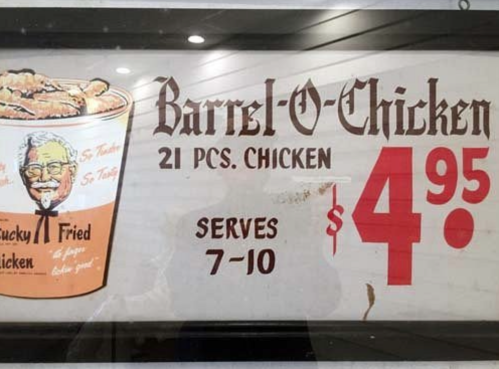 Sign advertising "Barrel-O-Chicken" with 21 pieces for $4.95, serving 7-10 people. Features a bucket of fried chicken.