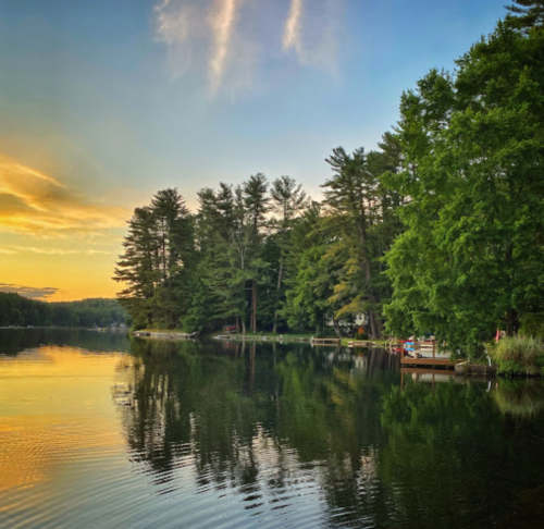A serene lake at sunset, surrounded by trees, with calm water reflecting the colorful sky.