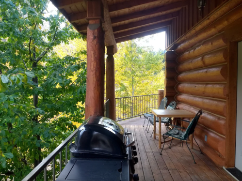 A wooden porch with a grill, table, and chairs, surrounded by trees and autumn foliage.