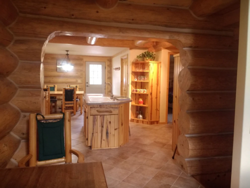 Cozy log cabin interior featuring a kitchen island, dining area, and wooden decor. Warm, inviting atmosphere.