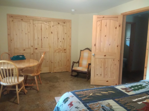 Cozy room featuring a quilted bed, wooden furniture, a round table, and a chair, with light-colored walls and doors.