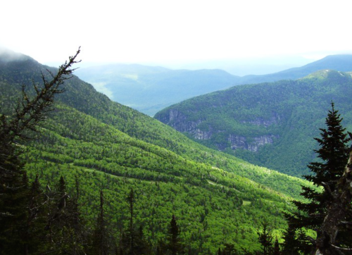 Lush green mountains and valleys under a cloudy sky, showcasing a serene natural landscape.