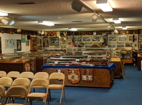 Interior of a museum display featuring military memorabilia, with glass cases and chairs arranged for visitors.
